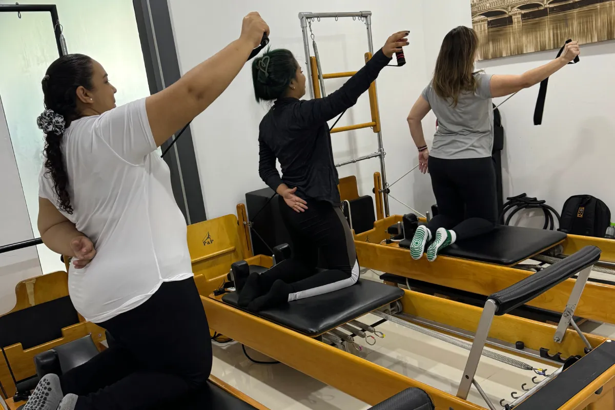 Tres mujeres realizando ejercicios con bandas en equipos Pilates Reformer
