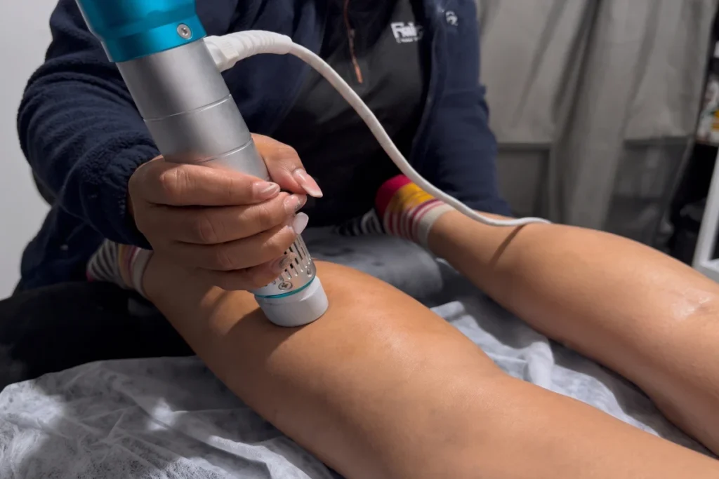 Fisioterapeuta aplicando un dispositivo de ondas de choque en la rodilla de una paciente