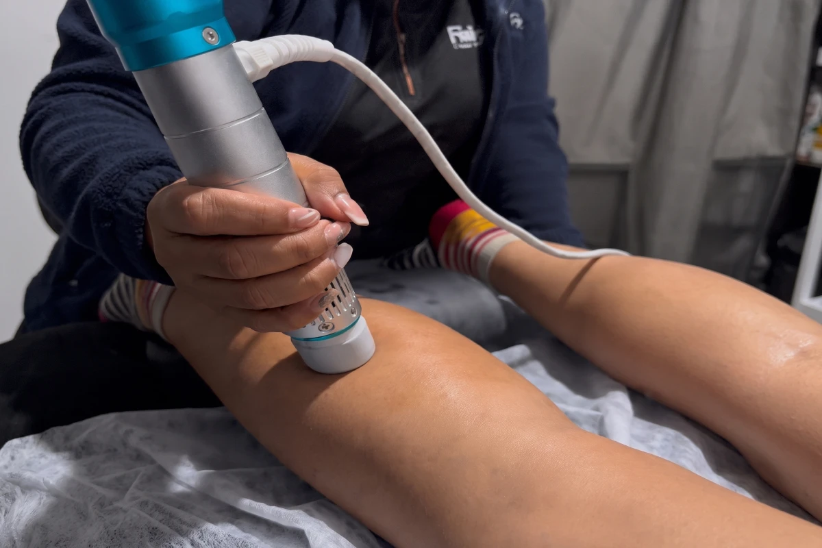 Fisioterapeuta aplicando un dispositivo de ondas de choque en la rodilla de una paciente