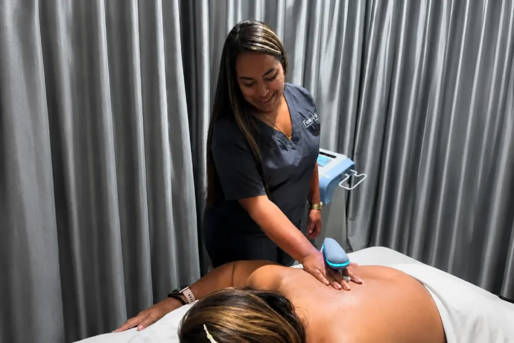 Fisioterapeuta aplicando un dispositivo terapéutico en la espalda de una paciente acostada