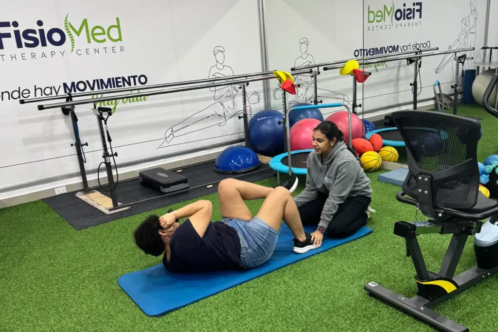 Paciente realizando un ejercicio abdominal sobre una colchoneta con apoyo de una fisioterapeuta
