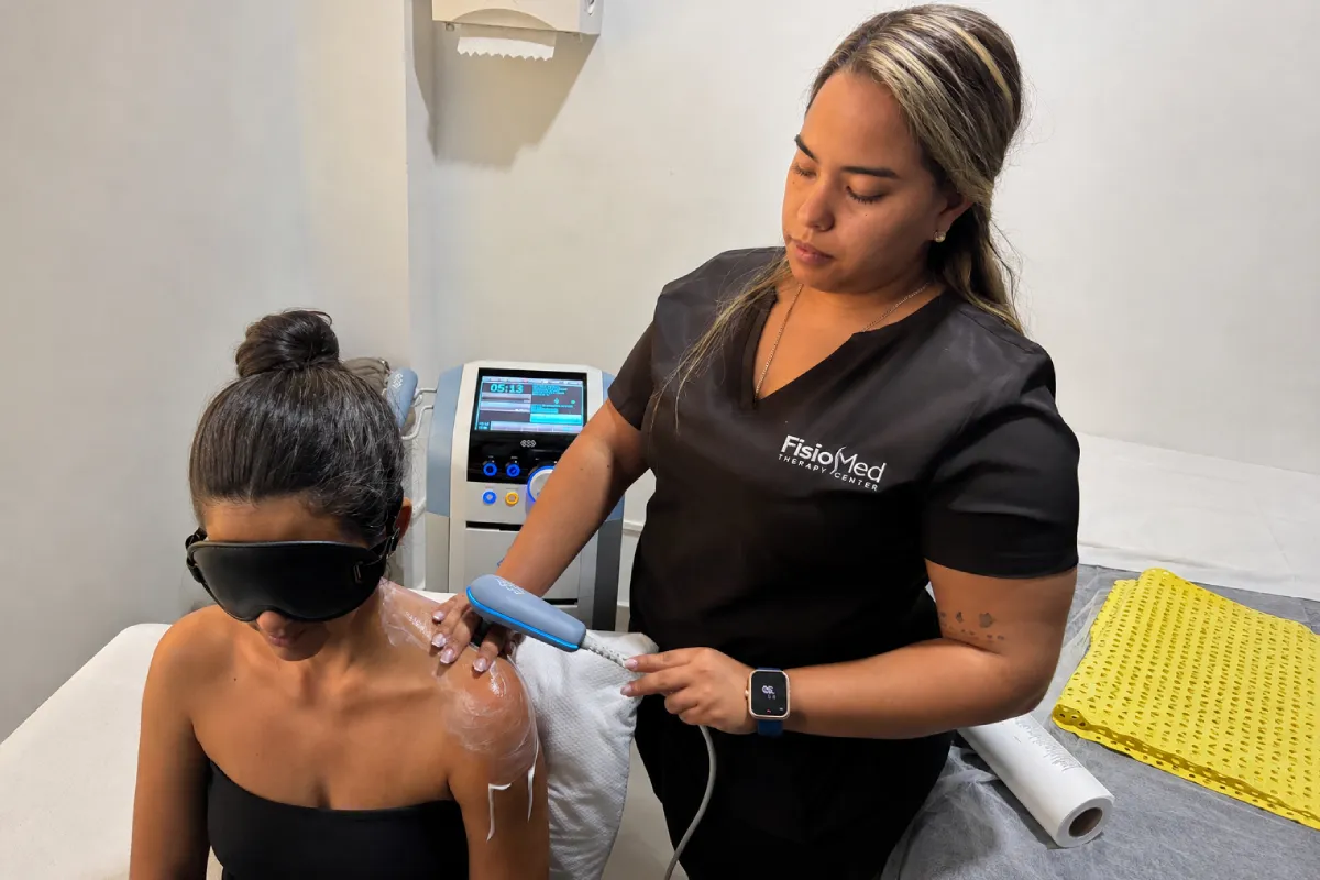 Fisioterapeuta aplicando un dispositivo terapéutico en el hombro de una paciente durante atención cervical