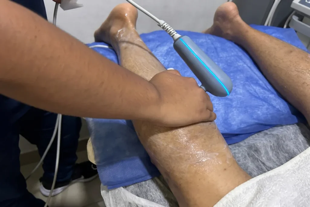 Fisioterapeuta aplicando un dispositivo terapéutico en la rodilla de un paciente