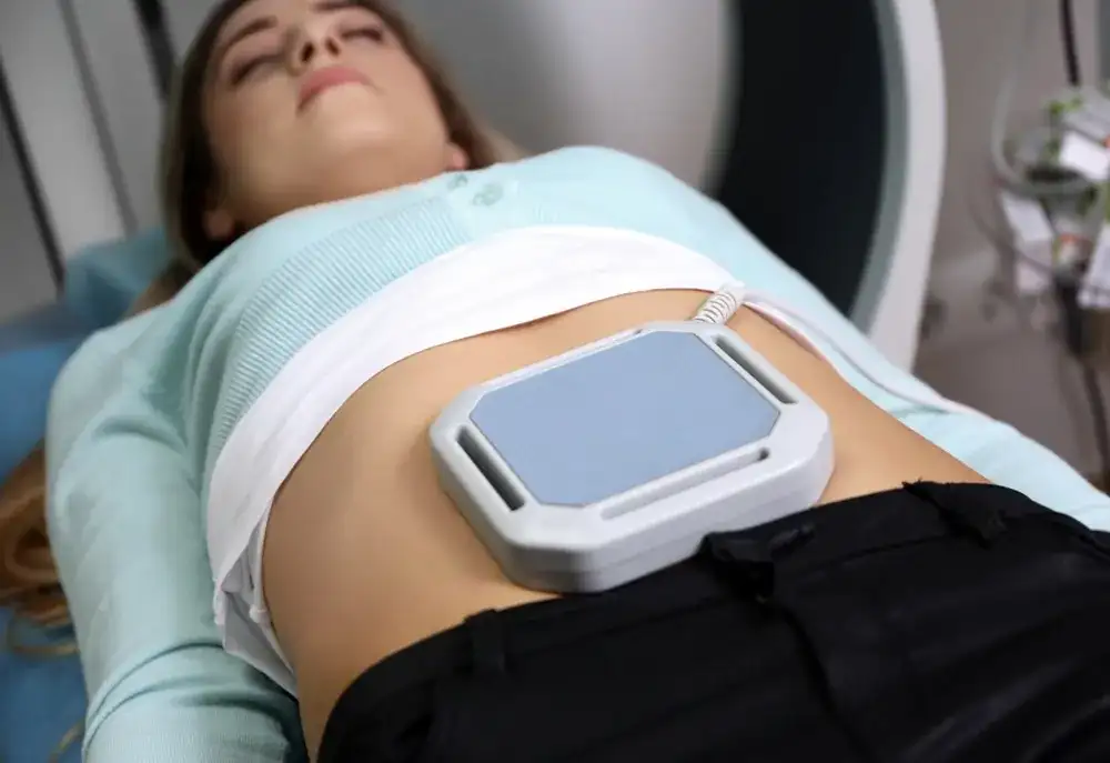 Paciente acostada con un aplicador de magnetoterapia sobre el abdomen