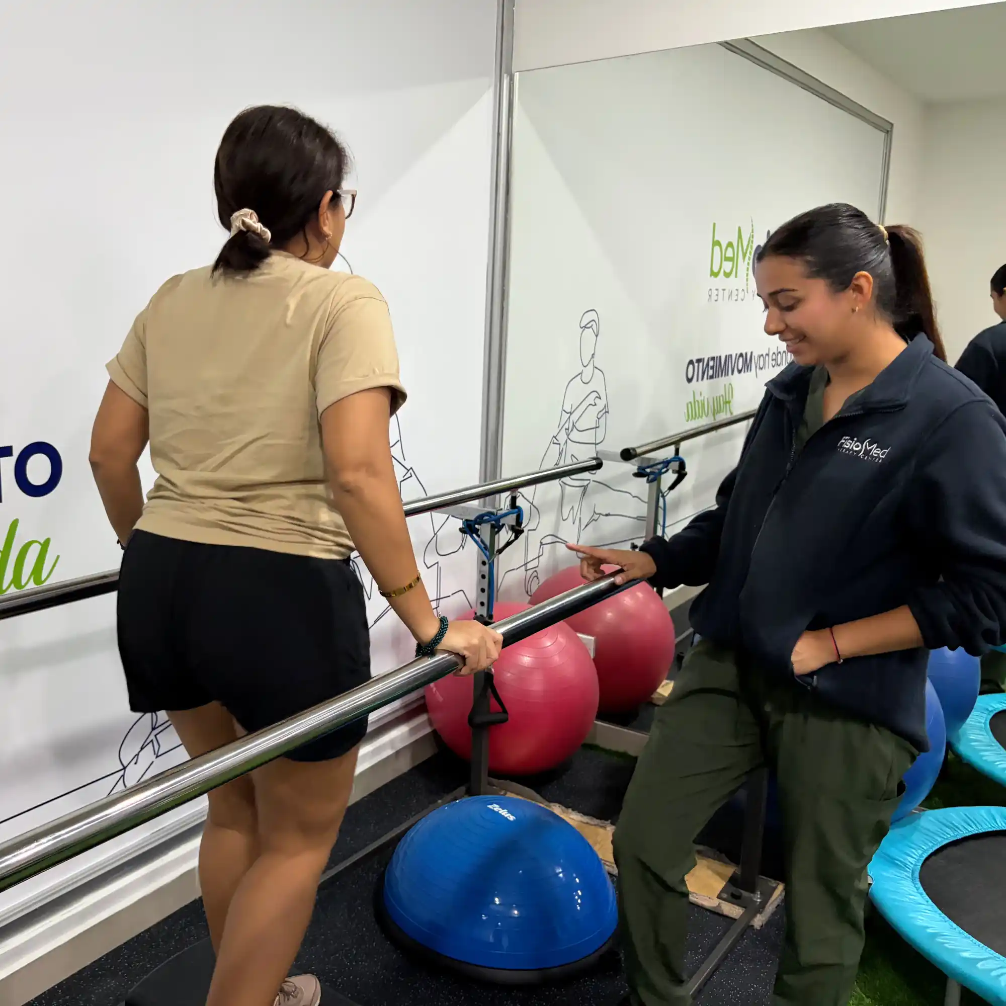 Paciente realizando un ejercicio en barras paralelas con supervisión de una fisioterapeuta